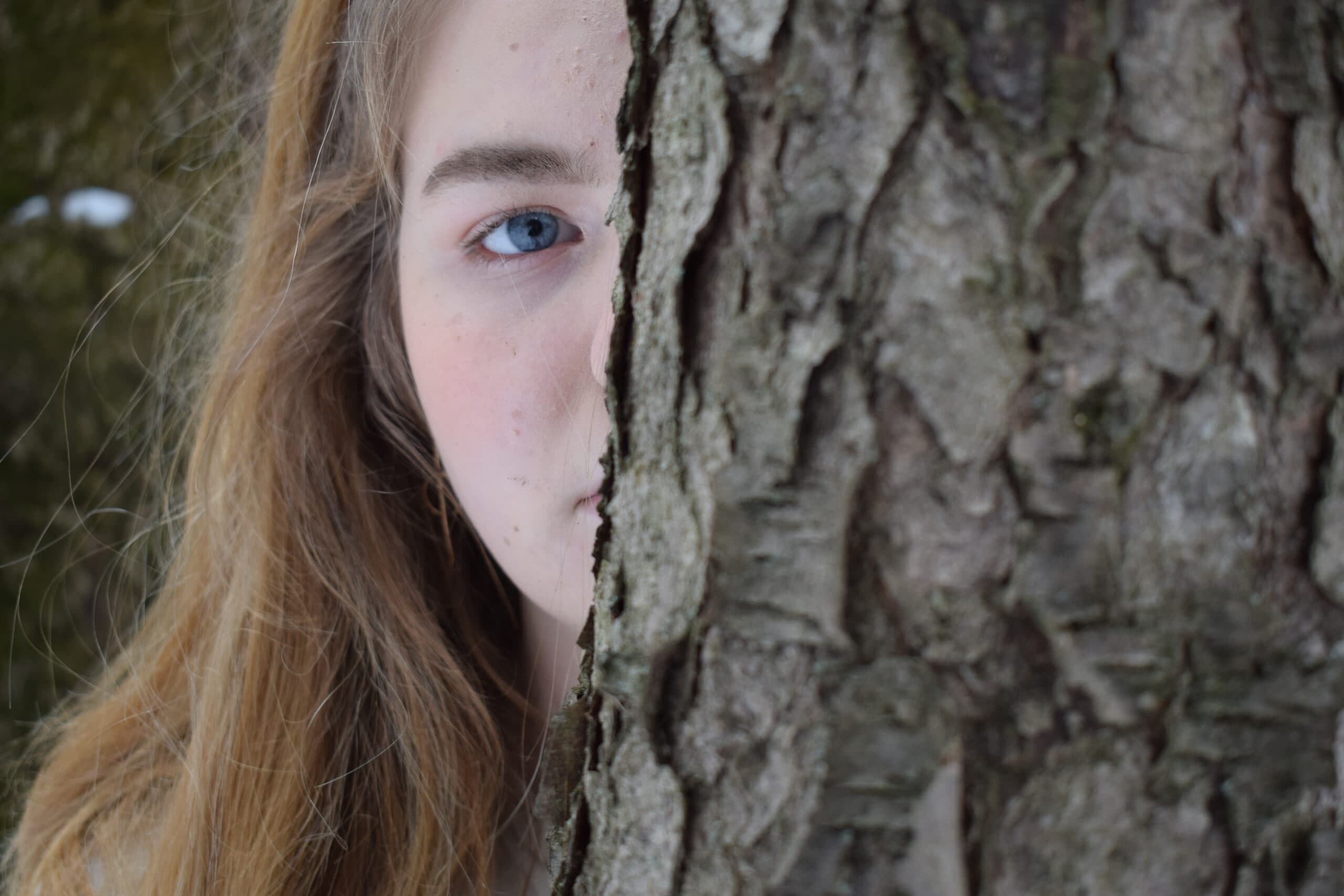 Creative portrait — a blue eye peeking from behind a tree